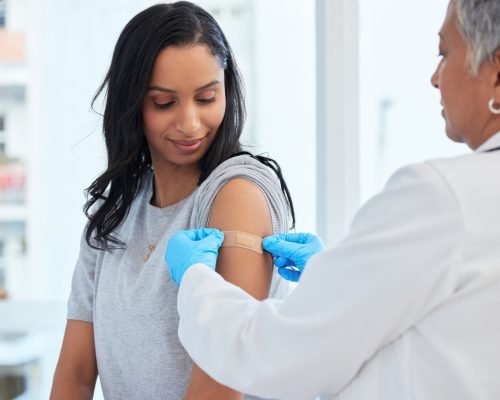 Healthcare, woman and doctor with plaster, vaccination and consultation in a hospital, cure and disease. Female patient, client and medical professional with band aid, care and injection for safety